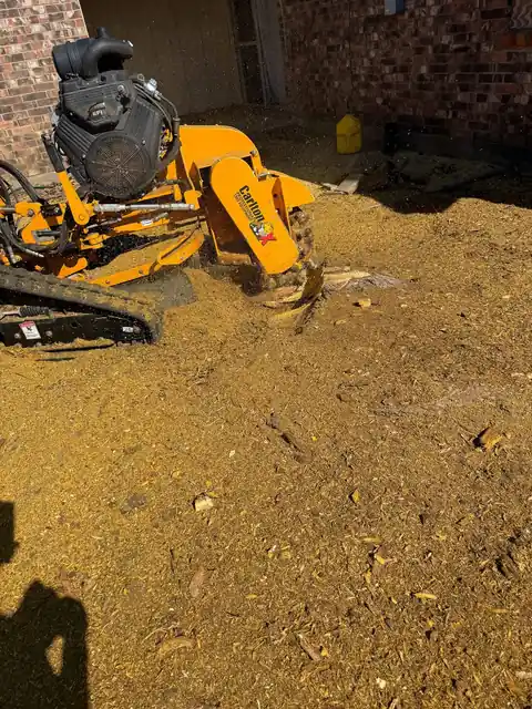 Tracked grinder by a brick wall throwing sawdust